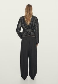 Černá kožená bunda s peplum lemem, opaskem a dlouhými rukávy. V kombinaci s černými širokými kalhotami s vysokým pasem.