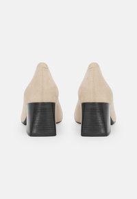 Beige velúr blokk sarkú cipők sima textúrával, hegyes orral és fekete fából készült sarkakkal, letisztult vonalakkal és minimális díszítéssel.