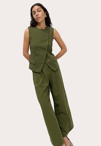 Gilet su misura verde oliva con design aderente, cinque bottoni e tasche laterali, abbinato a pantaloni a gamba larga a vita alta.