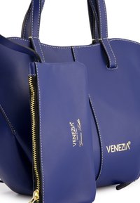 Blue leather handbag with structured shape, contrasting white stitching, and gold zipper accent on detachable pouch featuring brand logo.