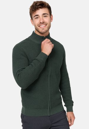 Cárdigan verde de punto con cremallera, que presenta un cuello alto, puños acanalados y un patrón texturizado. Hecho de un hilo grueso para proporcionar calidez.