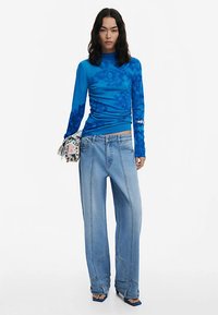 Sinine pika varrukaga särk lillemustriga, mille juurde on kombineeritud heledate toonidega laialt lõikega teksad, mis on kõrge vöökohaga ja millel on nähtavad õmblused.