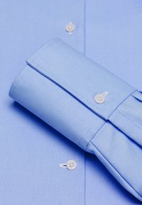 Lichtblauw overhemd met een gestructureerde stof, witte knopen en een opgerolde manchette. Beschikt over een klassiek button-down kraag en een gladde afwerking.
