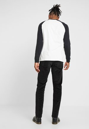Langemouwenshirt met een witte romp en zwarte raglanmouwen, gecombineerd met zwarte broek en zwarte laarzen. Gladde stof met een strakke pasvorm.