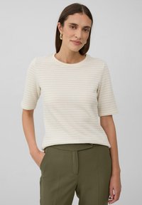 Haut beige clair texturé à manches courtes avec un col rond, associé à un pantalon tailleur vert olive. Le tissu présente un motif subtil.