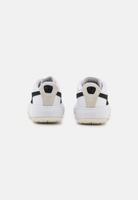 Baskets blanches avec un accent en daim texturé au talon, des rayures noires sur les côtés et une semelle en caoutchouc avec un logo au dos.