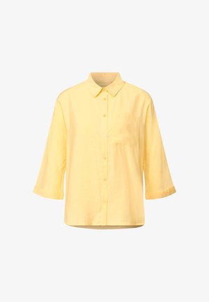 Gul skjorta med knappar och krage, trekvartslånga uppvikta ärmar och en enda bröstficka. Tillverkad av lättviktig tyg.