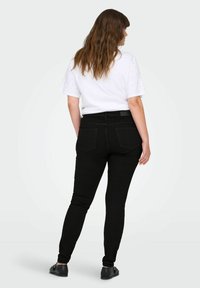 Fekete, skinny farmernadrág magas derékkal, öt zsebbel és sima textúrával, egy fehér, rövid ujjú inggel párosítva, amely diszkrét díszítésekkel rendelkezik.