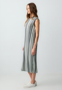 Ärmelloses Kleid mit vertikalen Streifen in Marineblau und Creme, weicher Stoff, A-Linien-Schnitt, fällt knapp unter die Knie, kombiniert mit weißen Sneakern.