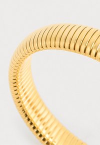 Gold-colored metal bracelet with a continuous ribbed texture, featuring a smooth, shiny surface and a circular shape.