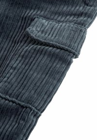 Gros plan sur un tissu en velours côtelé gris foncé avec des rainures verticales visibles et un détail de revers plié sur une manche ou une jambe de pantalon.
