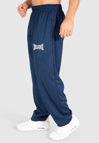 Marineblauwe sweatpants van textiel met een elastische tailleband, zijzakken en een wit geborduurd logo aan de voorkant.