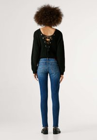 Mustast kootud kampsun pitsilise tagumise paela disainiga, kombineeritud siniste kitsaste teksadega. Teksadel on tagataskud ja need on keha järgi lõigatud.