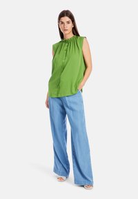 Grüne ärmellose Bluse mit gerafftem Halsausschnitt kombiniert mit hellblauen weit geschnittenen Hosen, die eine lässige Passform und eine weiche Stoffstruktur aufweisen.