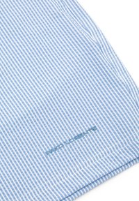 Jasnoniebieska koszula w białe paski z gładką fakturą, przeszyty dół i haftowane logo w ciemnoniebieskim kolorze w pobliżu dolnej krawędzi.