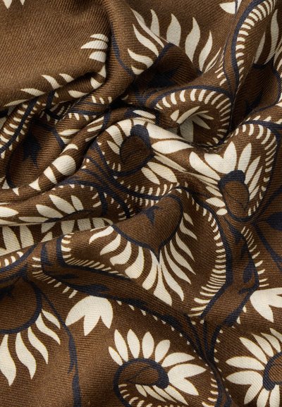 Καφέ ύφασμα με κρεμ και μαύρα λουλουδένια και φυλλώδη σχέδια, εμφανιζόμενο σε απαλά πτυχώσεις που αναδεικνύουν την υφή και τις λεπτομέρειες.