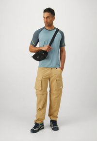 T-shirt desportiva azul-cinza com detalhes em néon, calças cargo bege com vários bolsos e mala preta tiracolo; combinadas com sapatilhas atléticas azuis.