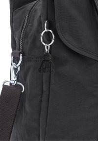 Sac en tissu noir avec fermeture éclair et poche à rabat, avec un petit porte-clés gorille noir attaché à un anneau en métal près de la fermeture éclair.