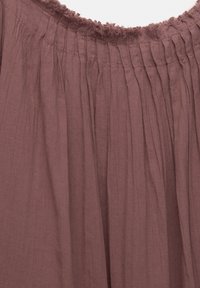Tissu mauve brunâtre avec taille élastiquée froncée et plis verticaux, montrant la texture et le détail du bord effiloché en haut.