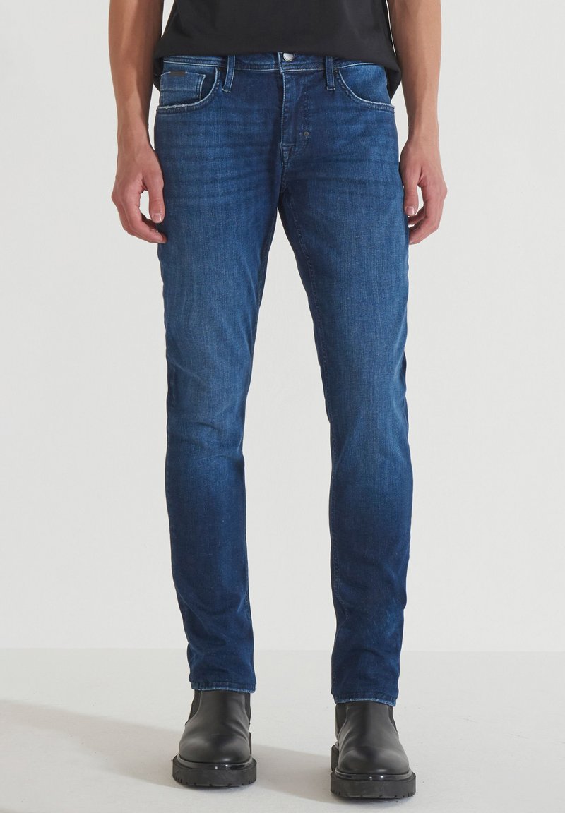 Jeans in denim blu scuro con vestibilità slim, design a cinque tasche, cuciture bianche a contrasto e dettagli consumati. Abbinati a stivali neri alla caviglia.