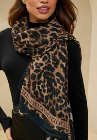 Leopardo raštuotas šalikas su rudos ir juodos spalvų schemomis, pagamintas iš lengvo materiolo, su akcentuotu krašto dizainu. Nešiojamas casual stiliumi.