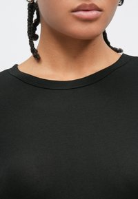 T-shirt preta de algodão com decote redondo. A textura parece lisa e macia, sem padrões ou desenhos visíveis.