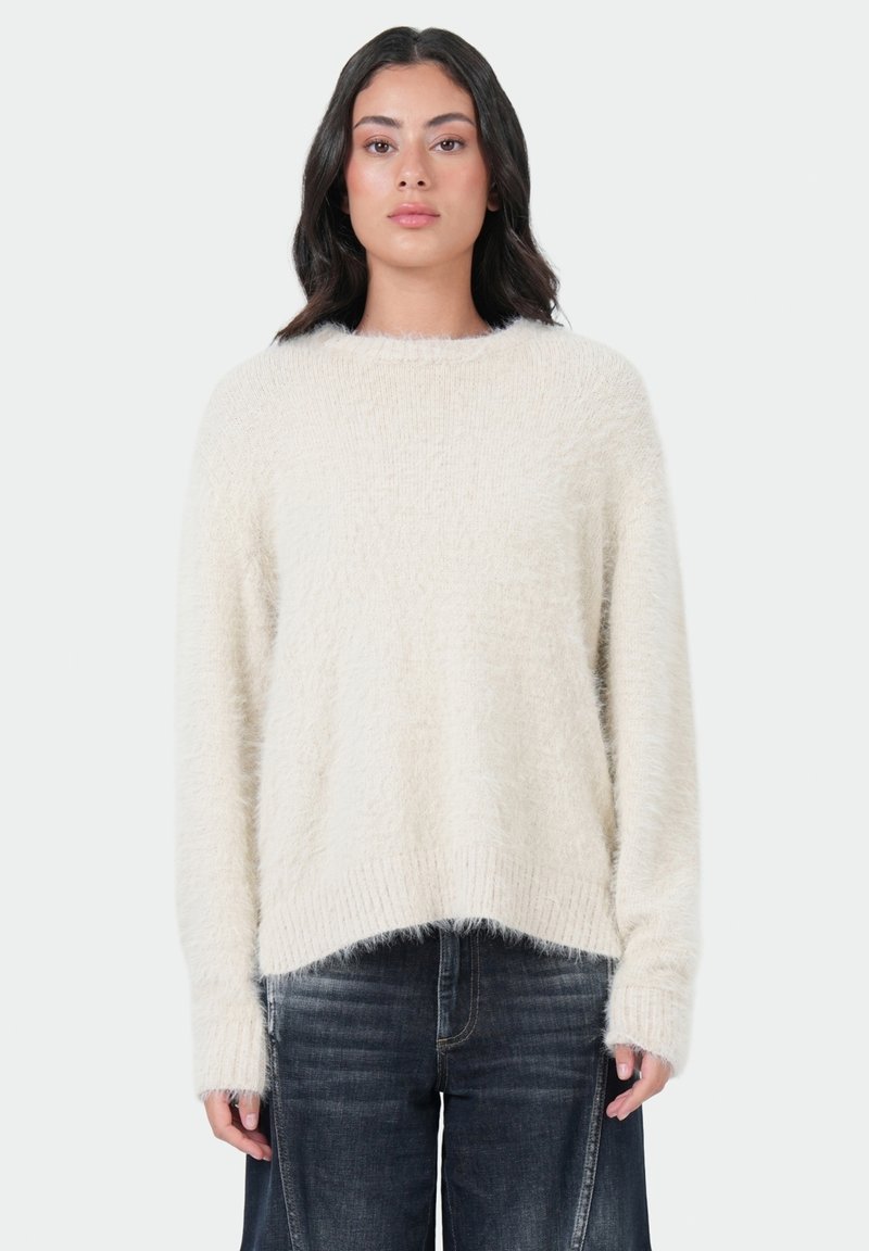 Crème-kleurige, pluche gebreide trui met lange mouwen, ronde halslijn en geribde onderrand, gecombineerd met donkere denim jeans.