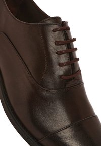 Chaussure habillée en cuir marron avec une finition lisse, bout arrondi, design à lacets à six œillets, et une délicate couture le long des coutures.