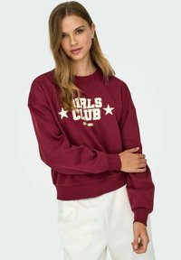 Burgundy sweatshirt featuring "GIRLS CLUB" text and stars in white, with a relaxed fit, ribbed cuffs, and soft fabric texture.