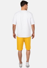 Witte t-shirt met korte mouwen gecombineerd met gele shorts tot op de knie. De stof lijkt glad met een losse pasvorm en subtiele stiksels.