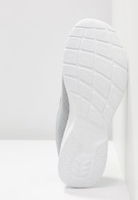 Semelle en caoutchouc blanche d'une chaussure de sport Skechers grise montrant des motifs de semelle géométriques sur un fond blanc uni.