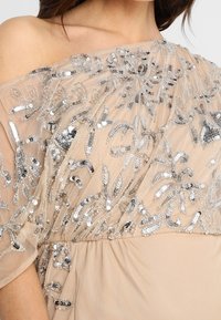 Beżowa sukienka bez ramiączek z haftem kwiatowym z srebrnych cekinów, przezroczystą powłoką i marszczonym pasem. Teksturowana tkanina z płynącym fasonem.