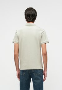 Világosszürke, rövid ujjú póló ing, sima anyagból, gallérral. Sötétkék farmernadrággal viselve, hátulról nézve.