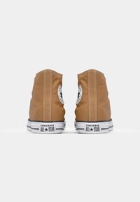 Bruine canvas high-top sneakers met witte rubberzolen, zwarte accenten en een zwart sterlogo aan de buitenkant, met zichtbare stikseldetails.