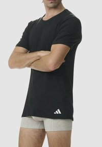 Maglietta nera a maniche corte con scollatura arrotondata, realizzata in tessuto morbido. Include un logo Adidas bianco sul lato sinistro in basso.