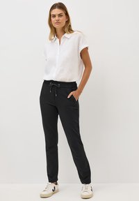 Hvid linned skjorte med kortærmer og knaplukning, parret med sorte tapered bukser med elastisk talje og snøring. Sneakers fuldender looket.