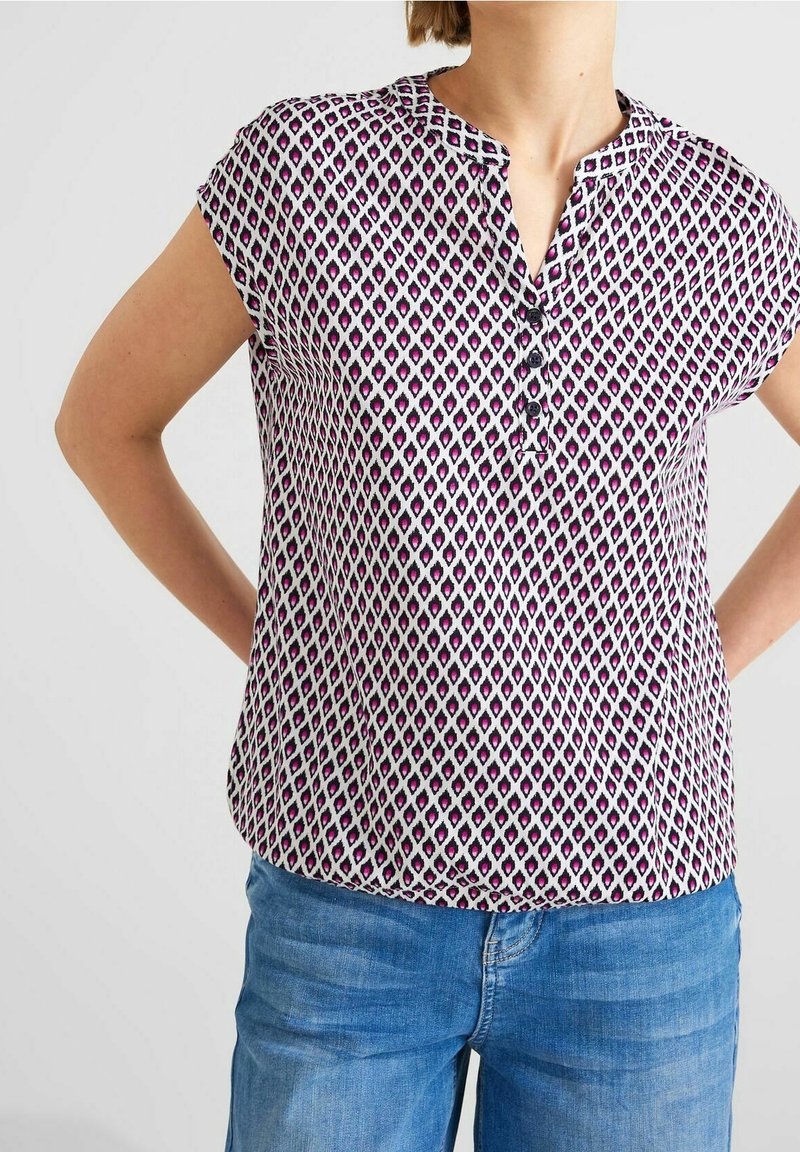 Blusa a maniche corte con scollo a V, caratterizzata da un motivo geometrico in viola e bianco, dettagli con bottoni e vestibilità morbida. Realizzata in tessuto leggero.