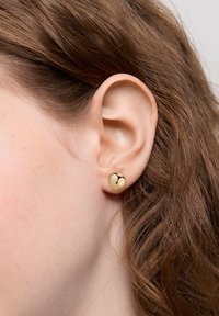 Okrągłe kolczyki stud w kolorze kremowym z czarnym abstrakcyjnym wzorem. Wydają się gładkie, są umocowane na widocznym metalowym słupku.