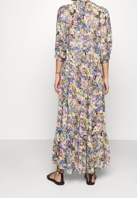 Robe maxi florale avec un motif multicolore comportant des fleurs roses, jaunes et bleues sur un fond vert. Manches longues et ourlet à volants.