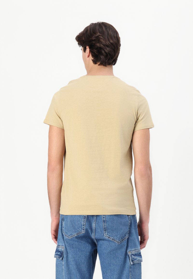 Camiseta de algodón de manga corta y cuello redondo en color beige claro, con una textura suave y lisa y un diseño sencillo y ajustado. Sin gráficos visibles.