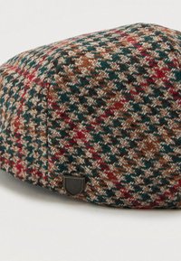 Căciulă plată cu un model houndstooth în nuanțe de verde, maron, bej și roșu, având un mic emblema în formă de scut negru pe lateral.