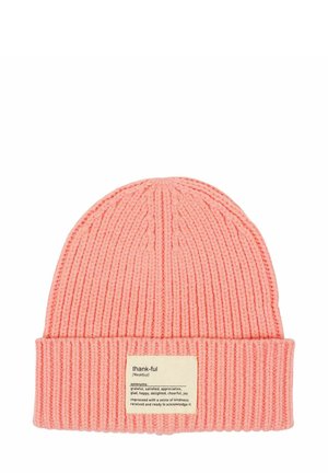 Pink knitted beanie with a folded brim, featuring a fabric label with the word "thank-ful" and synonym definitions attached.