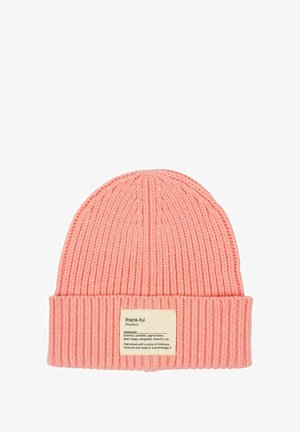 Pink knitted beanie with a folded brim, featuring a fabric label with the word "thank-ful" and synonym definitions attached.