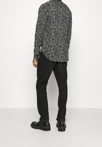 Camicia a righe bianco e nero con vestibilità morbida, maniche lunghe, colletto button-down, abbinata a pantaloni neri e stivali.