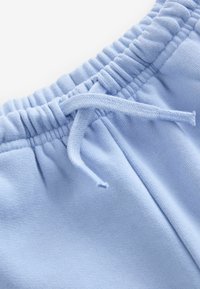 Pantalons de jogging bleu clair avec une taille élastique, dotés d'un cordon de serrage et d'une texture douce, présentés en gros plan pour mettre en valeur les détails du tissu.