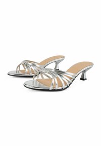 Srebrne sandały na obcasie z paskami, odkrytymi palcami i niskimi, zakrzywionymi obcasami oraz beżowymi wkładkami, pokazane z boku na białym tle.