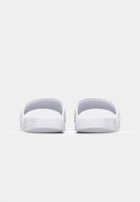 Baskets blanches à enfiler avec un dos ouvert et une semelle texturée. Matériau lisse avec un design minimaliste et aucune marque visible.