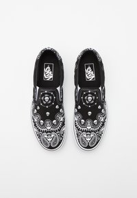 Black slip-on shoes with a white skull and paisley pattern, featuring a smooth canvas material and white rubber soles.