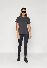 Μαύρο αθλητικό Τ-shirt με μπλε λογότυπο στο αριστερό στήθος, συνδυασμένο με μαύρο κολάν και μαύρα αθλητικά παπούτσια. Άνετη εφαρμογή, λείο ύφασμα.