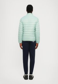 Jachetă pufoasă de un verde mentă deschis, cu quilting orizontal, asortată cu pantaloni de trening bleumarin. Textură netedă, guler în picioare și fără logo-uri vizibile.